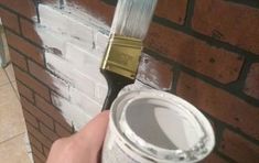 a person holding a paintbrush in front of a brick wall with white paint on it