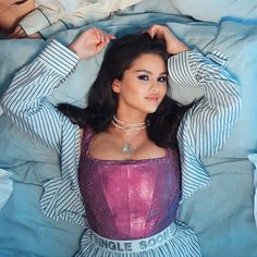 a woman laying on top of a bed wearing a purple dress and pearl choker