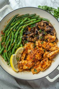 chicken, green beans and mushrooms in a skillet with lemon wedges on the side