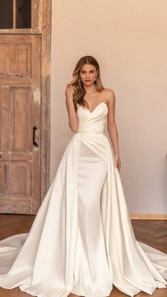 a woman standing in front of a piano wearing a wedding dress with an asymmetrical neckline