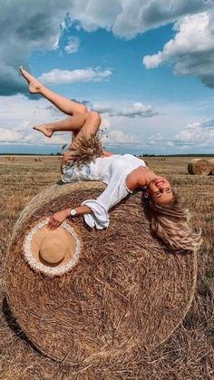 a woman laying on top of a hay bale in the middle of a field