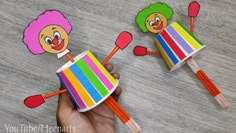 someone is holding two colorful pencils with clown faces on them and one has a pink hair