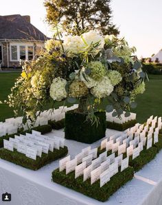 an arrangement of white flowers and greenery on a table with seating cards for guests