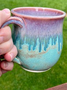 a hand holding a blue and purple coffee cup on top of a wooden table outside