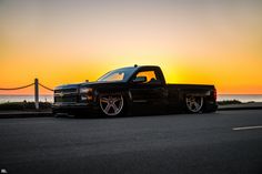 the truck is parked on the side of the road near the ocean at sunset or dawn