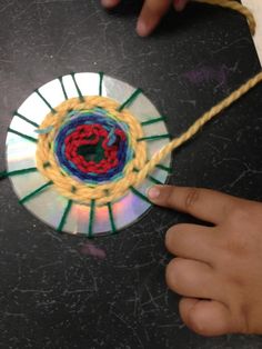 a person is holding a cd in front of a circular object with yarn on it