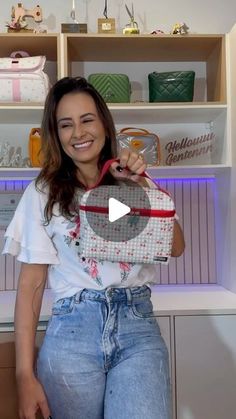 a woman is holding a purse in her hands and smiling at the camera while standing next to some shelves