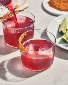 two glasses filled with red liquid and garnished with gold flecks sit on a table