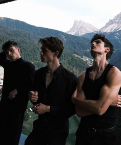 three men standing next to each other with mountains in the background