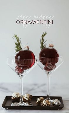 two glasses filled with red liquid and gold ornaments on a tray that says very merry ornamentii