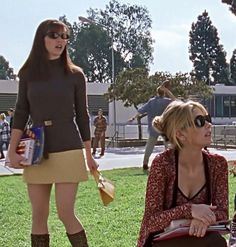 two women sitting on the grass in front of a group of people wearing sun glasses