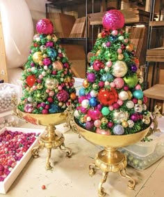 two christmas trees sitting on top of gold trays filled with balls and other ornaments