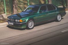 a green car is parked on the side of the road next to a fence and trees