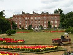 a large brick building with lots of flowers in the foreground and a garden area on the other side