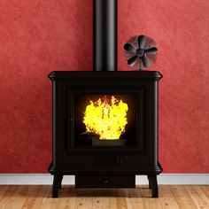 a black stove with yellow flames in front of a red wall and wooden flooring