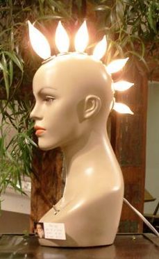 a white mannequin head with lights on it's head and leaves in the background