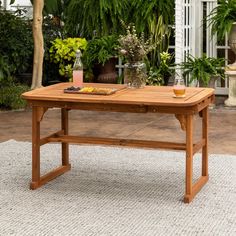 a wooden table sitting on top of a white rug next to potted plants and trees