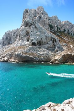 a boat is in the clear blue water near a rocky mountain range with an island behind it