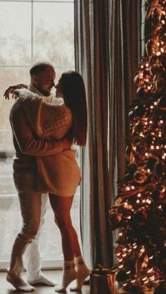 a man and woman standing in front of a christmas tree with their arms around each other