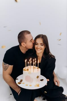 a man and woman kissing while holding a cake with lit candles