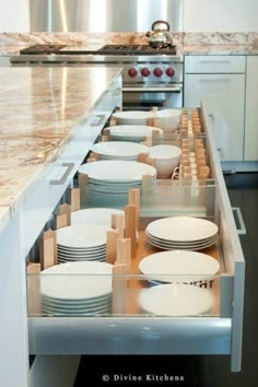 an open drawer in the middle of a kitchen with plates and bowls on it's sides