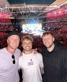 three men standing next to each other in front of an arena full of people at a concert