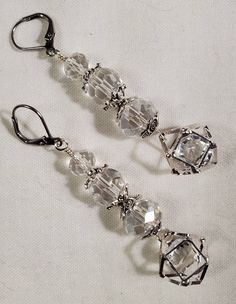 Crystal Cages is a stunning pair of crystal earrings with a set of 3 crystals of various sizes, terminating in a Jesse James caged crystal. The cage is silver-toned with silver-toned bead caps. They are hanging from stainless steel leverback earwires. They hang approximately 2 inches in length. The Cage, Jesse James, Bead Caps, Crystal Earrings, Beautiful Earrings, Jewelry Earrings Dangle, Silver Bracelet, Dangle Drop Earrings, Silver Tone