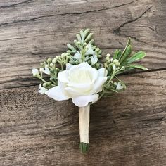 a boutonniere with white flowers and greenery on a wooden table top