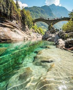 people are standing on a bridge over clear water