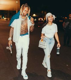 a man and woman walking down the street at night with one holding a cell phone