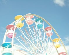 the ferris wheel is brightly colored and stands in front of a blue sky with clouds