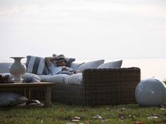 a man sitting on top of a wicker couch next to a table with pillows