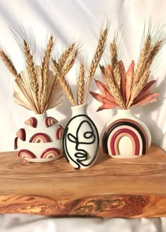 three vases with different designs on them sitting on a wooden table next to wheat stalks