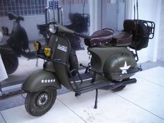 a green motorcycle parked in front of a building with two people looking at it from the window