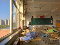 an empty classroom with lots of desks and chairs in front of a window overlooking the city