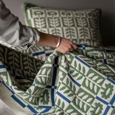 a person holding onto a green and white blanket on top of a bed next to pillows