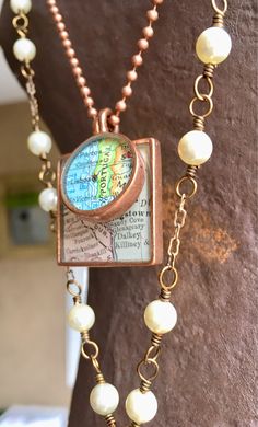 a close up of a necklace with pearls and a map on it's chain