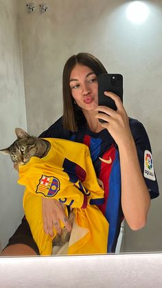 a woman taking a selfie with her cat in a soccer jersey while holding a cell phone