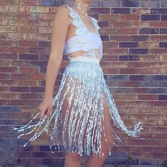 a woman standing in front of a brick wall wearing a blue and white fringe skirt