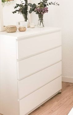 a white dresser with flowers in vases on top