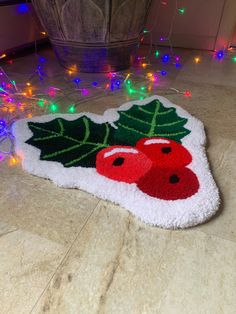 a white rug with holly and cherries on it next to christmas lights in the background