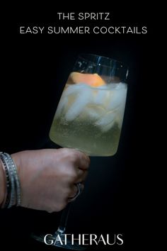 a hand holding a wine glass filled with ice and lemonade on top of a black background