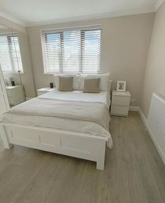 a white bed sitting in a bedroom next to a window with blinds on the windowsill