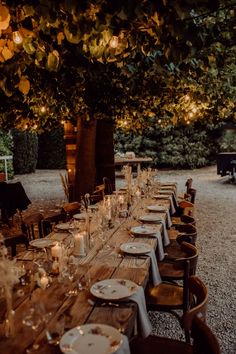 a long table set up with place settings and lit candles for an outdoor dinner party