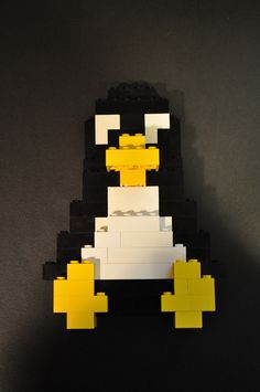 a lego penguin with yellow and white blocks on it's back legs, sitting in front of a black background