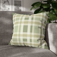 a green and white checkered pillow sitting on top of a couch next to a potted plant