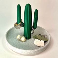 three green cactus shaped objects on a white plate with pearls and rings around them, including an earring holder