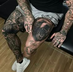 a man with tattoos on his legs sitting in a chair