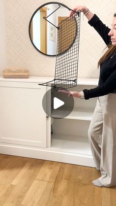 a woman standing in front of a mirror holding a wire basket over the back of a chair