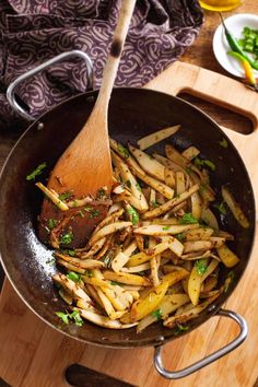 french fries being cooked in a skillet on a cutting board with a wooden spoon